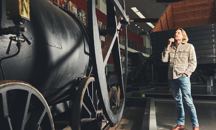 A man looks at a large black engine. It's a replica of Richard Trevithick's steam locomotive, the first steam powered vehicle to run on rails in 1804.